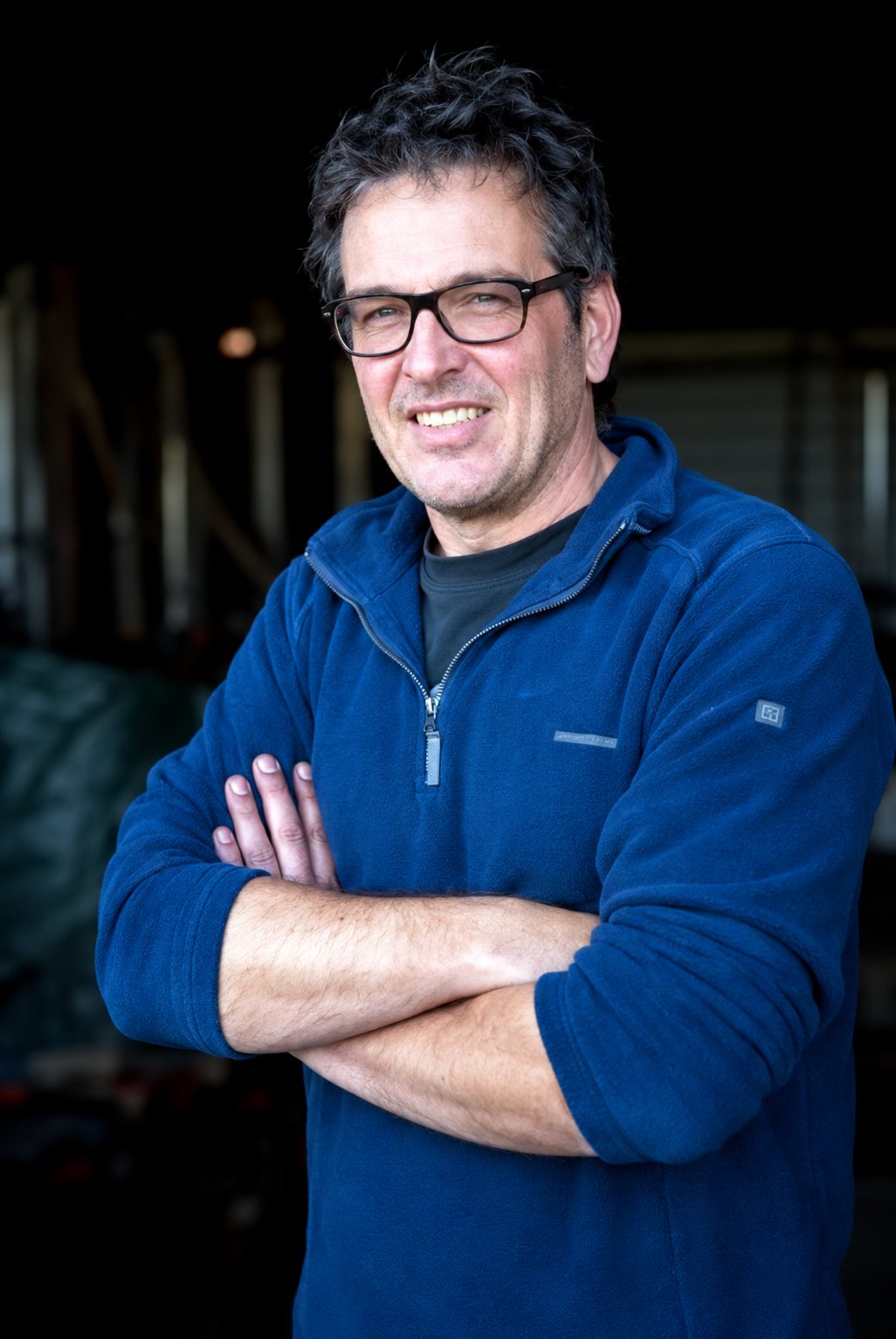 Portrait of a smiling man with glasses, arms crossed.